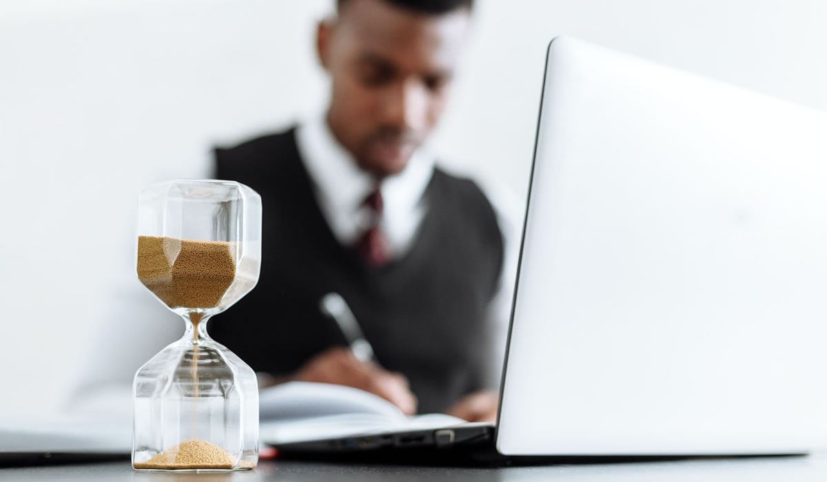 Man writing on laptop with a sand hourglass on the desk