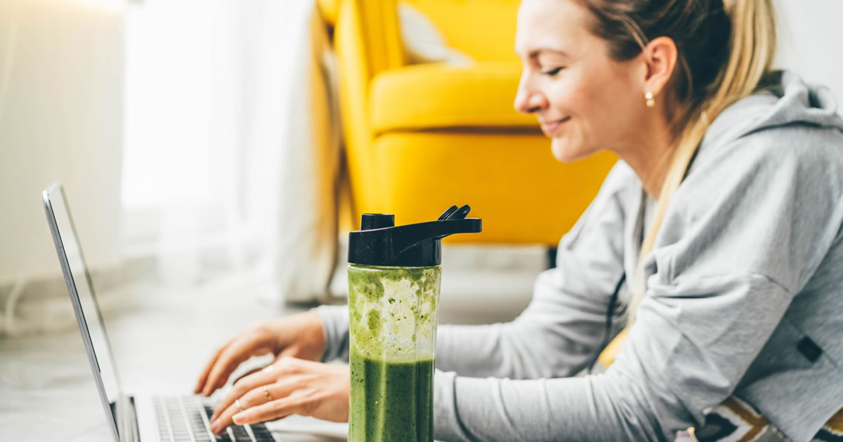 Smiling woman typing on laptop next to green smoothie
