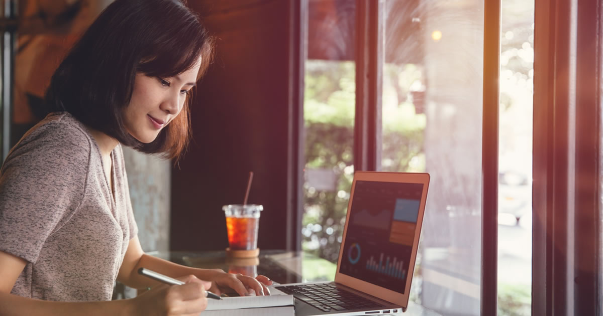 Uma mulher freelancer trabalhando em um projeto com laptop e caderno de anotações em um café