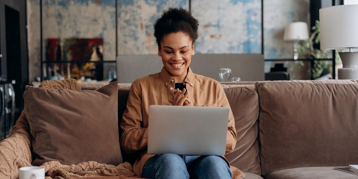 Jovem feliz escrevendo no laptop, sentada no sofá