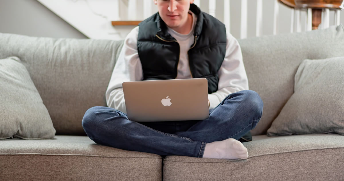 Young man sitting on couch writing on laptop