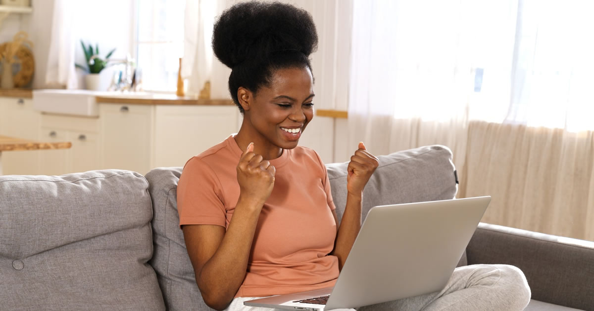 Excited millennial woman sitting on couch looking at laptop computer