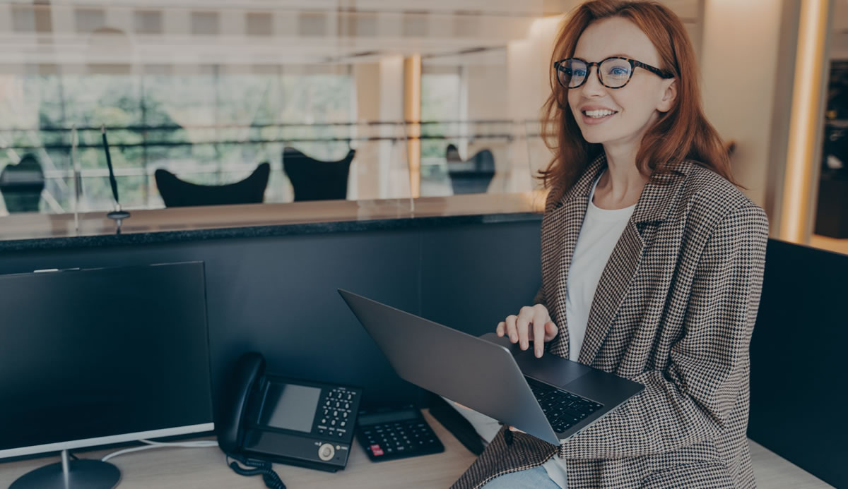 Businesswoman sitting in her office cubicle while holding laptop and smiling