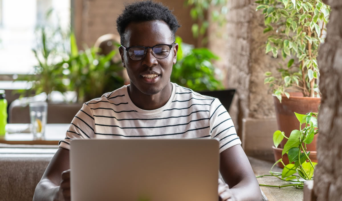 Smiling man in striped shirt and eyeglasses using laptop at restaurant table