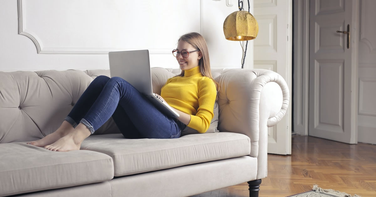 woman on sofa, writing on laptop