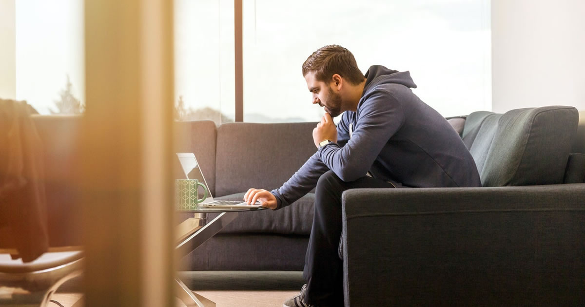 Homem usando laptop, pensando profundamente, sentado no sofá