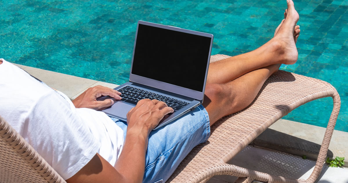 Male freelance writer relaxing poolside, writing on laptop