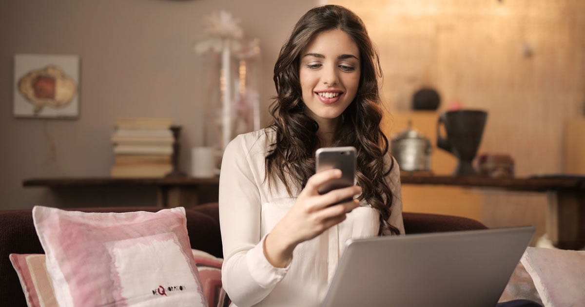 Mulher feliz sentada em um sofá com laptop jogando no smartphone