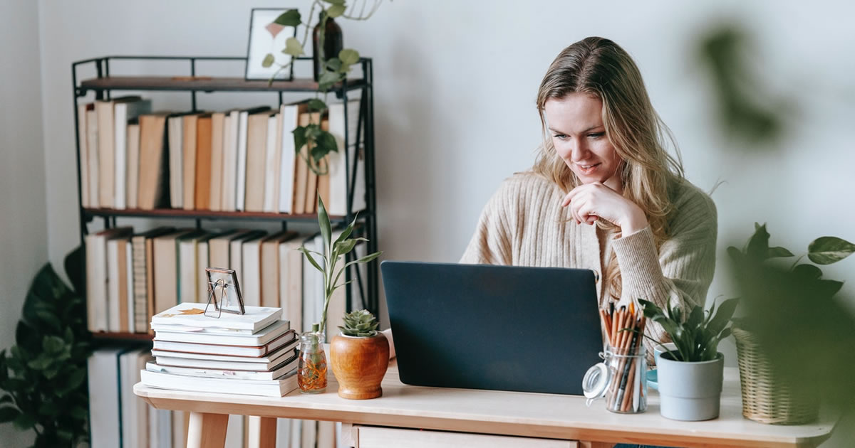 smiling blonde freelance writer looking at laptop at home desk