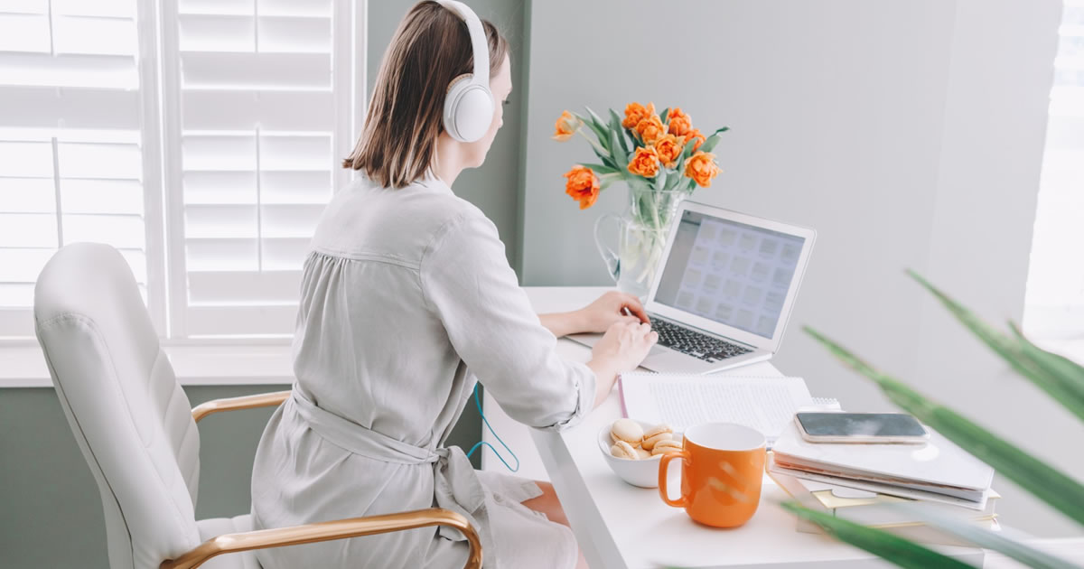 Woman in headphones writing on laptop in home office