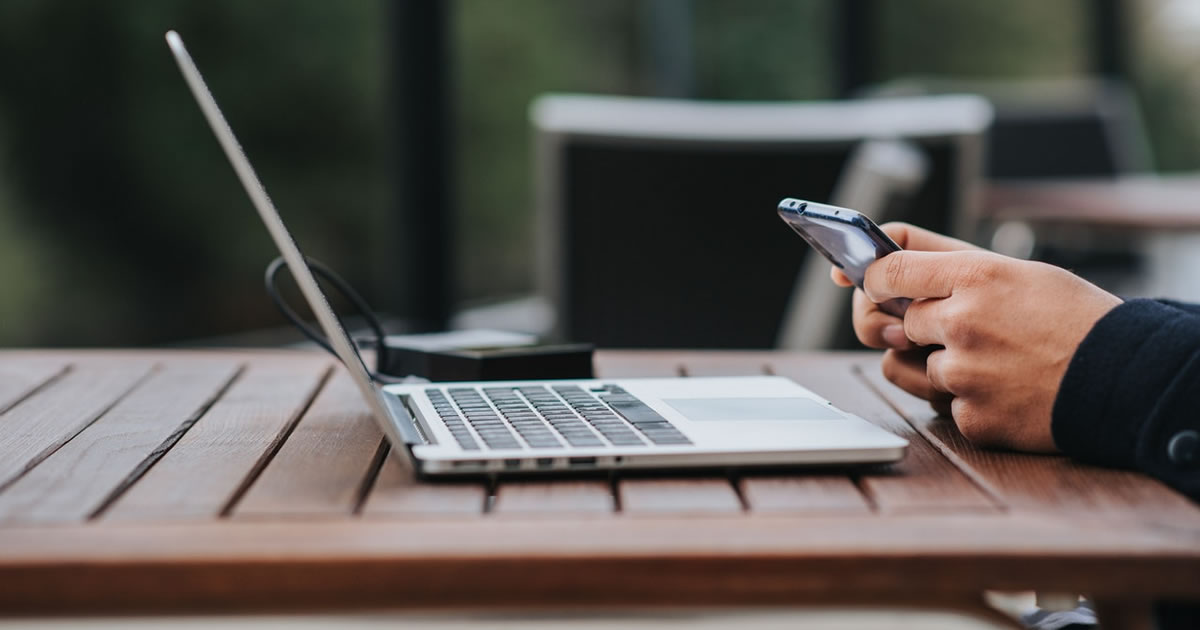 Empresário envia mensagens de texto pelo smartphone em uma mesa com laptop