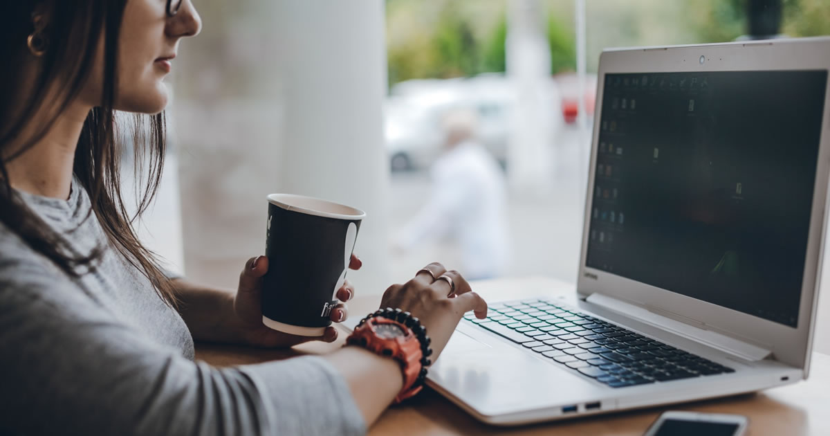 Jovem mulher de negócios com xícara de café trabalhando no laptop