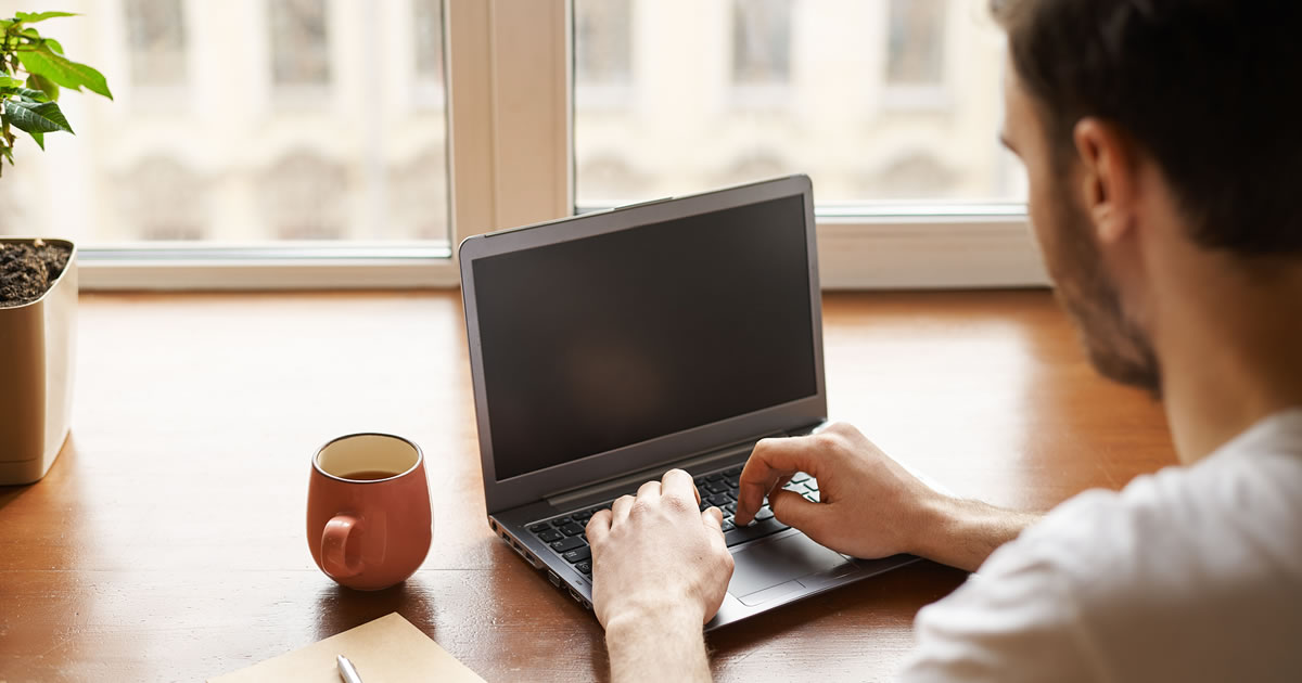 Back view of copywriter guy at desk writing copy or content on a laptop