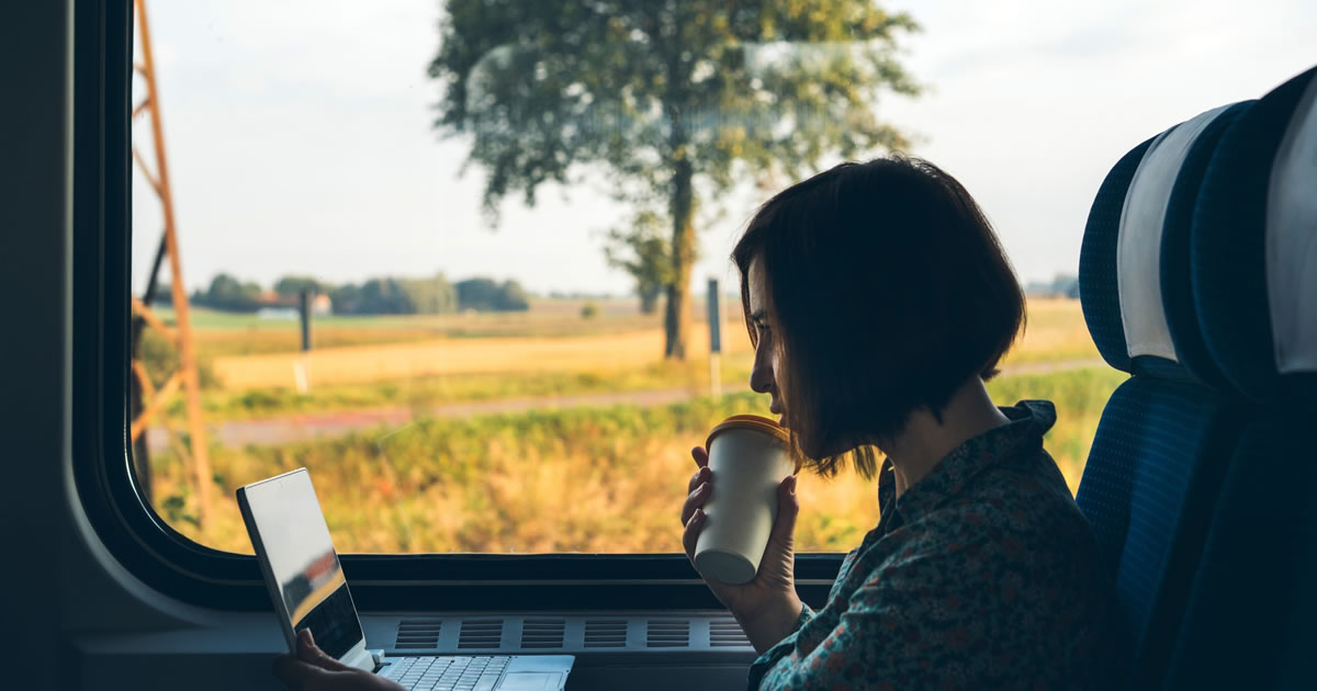 Uma escritora com um laptop sentada à janela de um trem