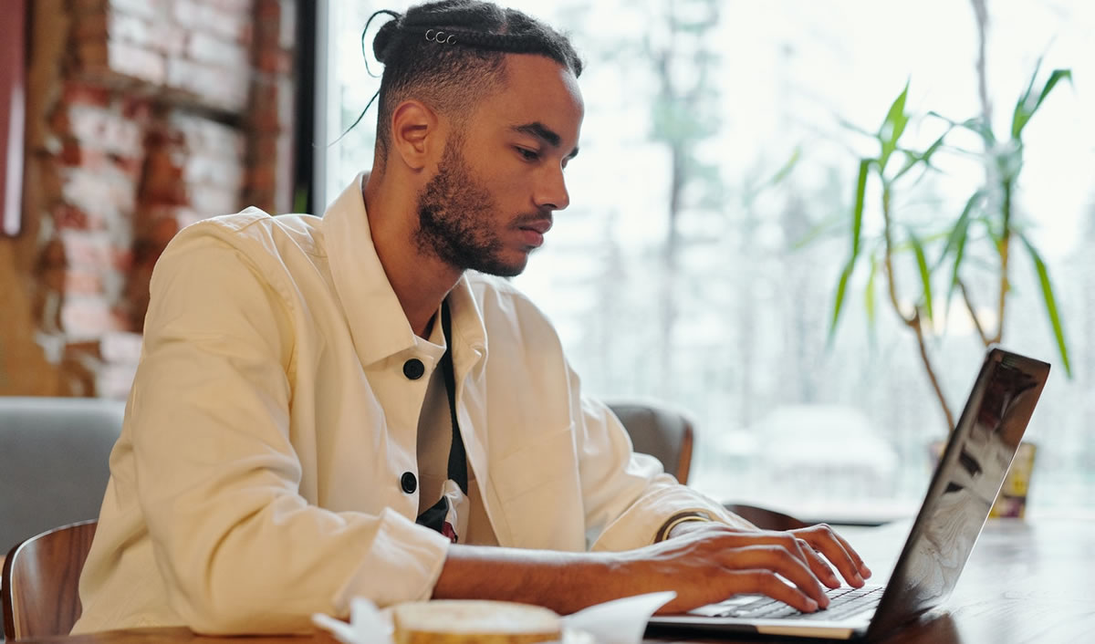 male freelance writer sitting at table writing on laptop