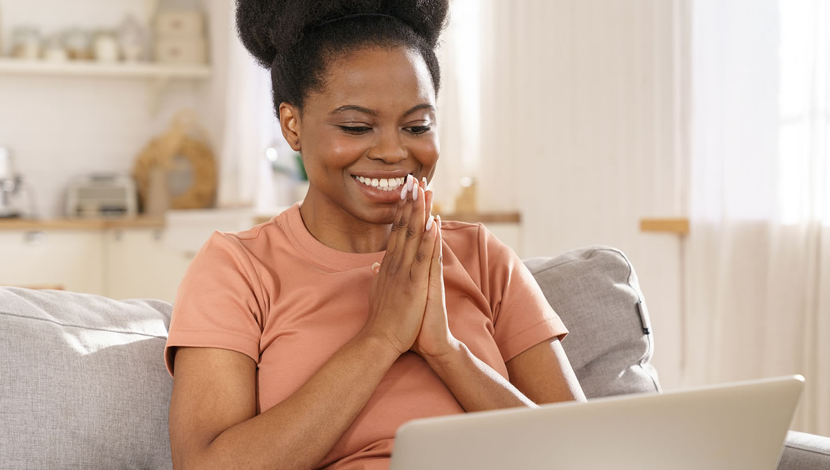Woman sitting on a sofa smiling while looking at her laptop