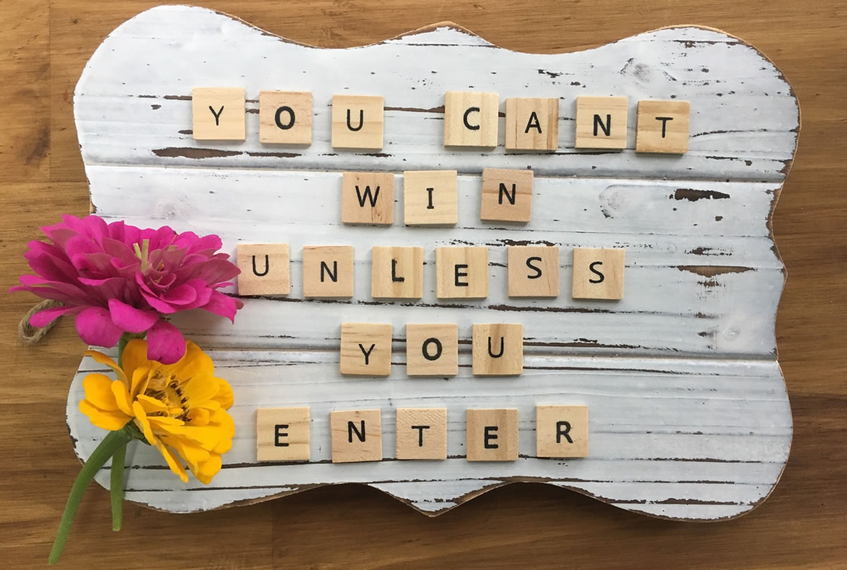 Wooden board with flowers next to wooden letter tiles spelling out the words you can't win unless you enter