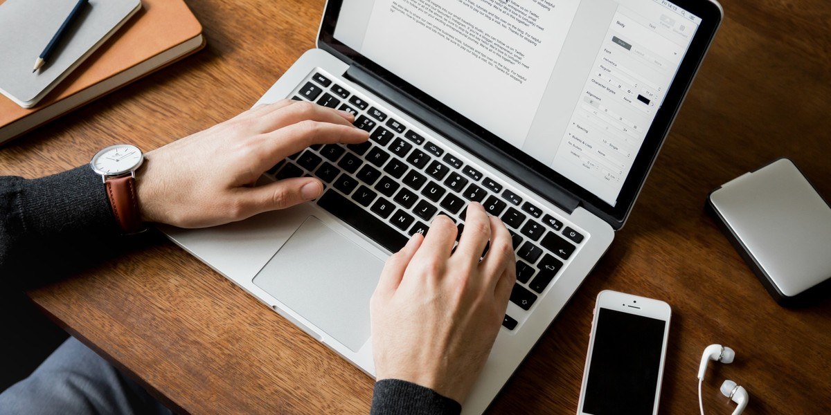 Man writing on a laptop at a wooden desk