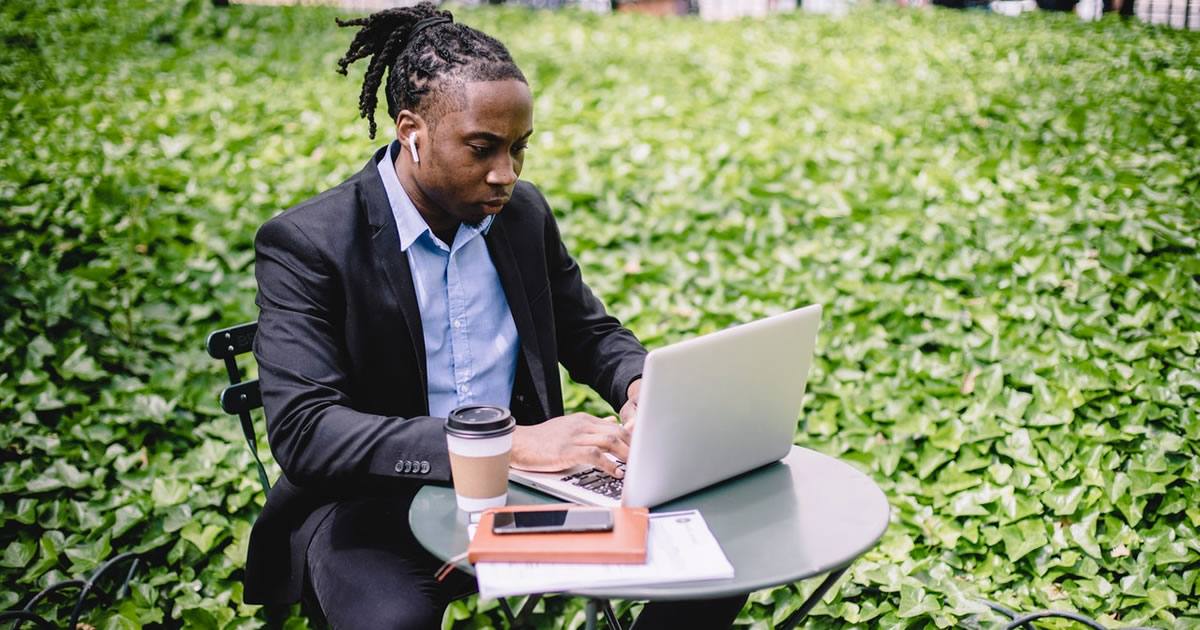 Homem escrevendo em um laptop em uma mesa externa