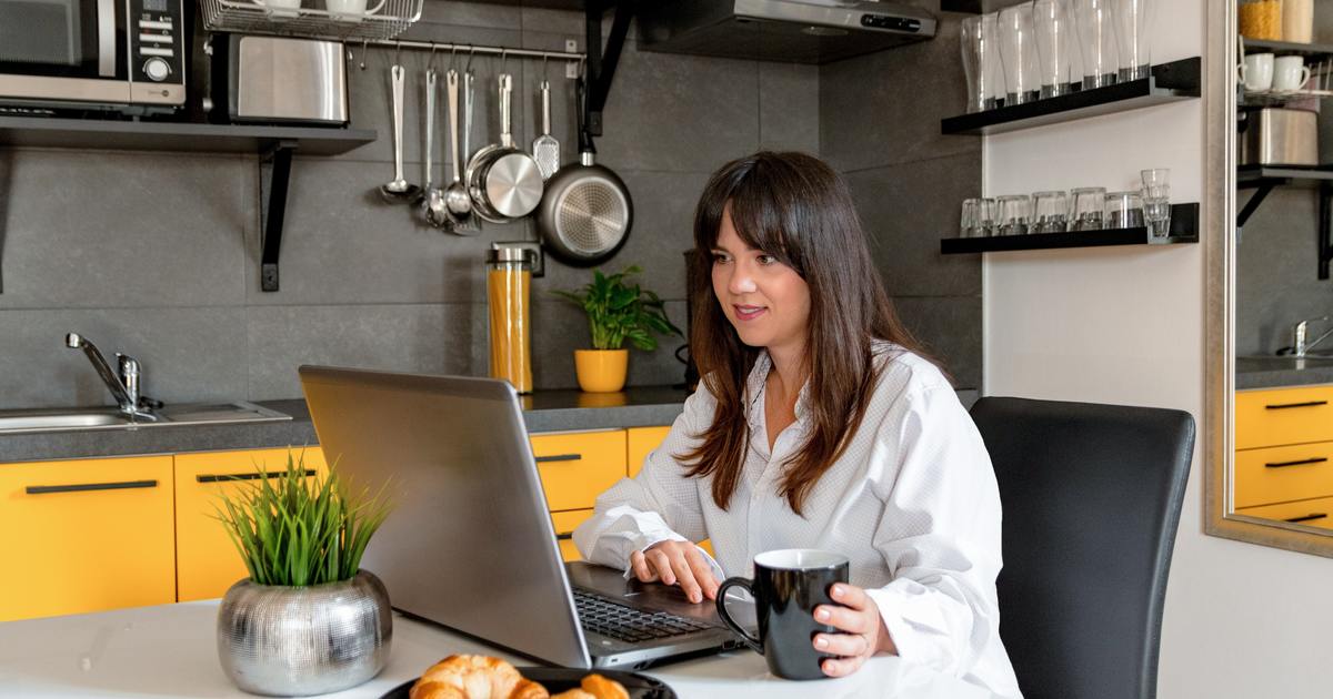 Woman working on laptop in the kitchen drinking coffee