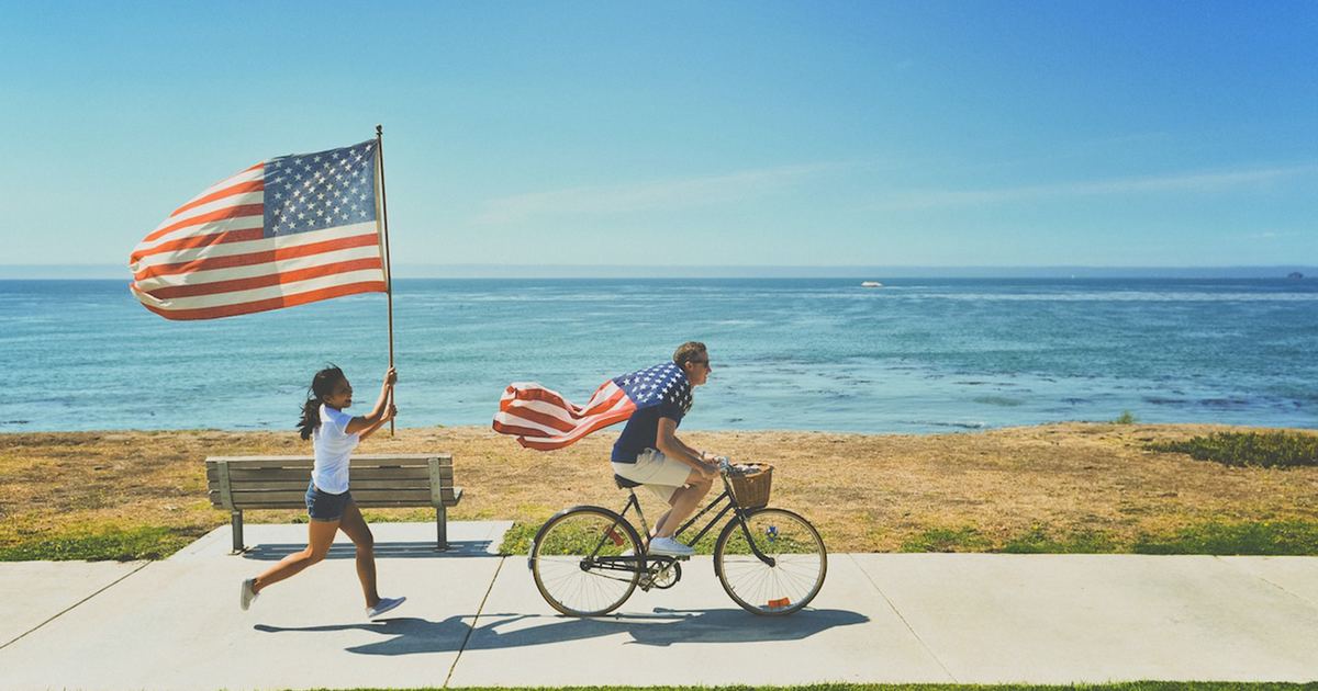 Girl running with american flag behind guy on bicycle
