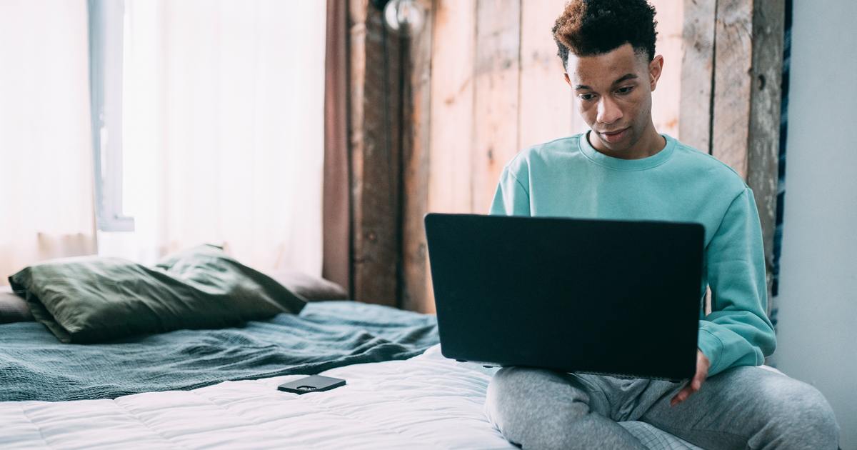 Man sitting on a bed typing on a laptop