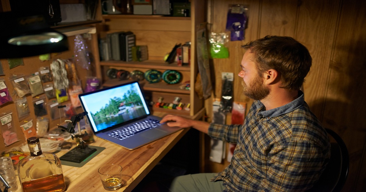 Escritor freelancer usando seu laptop enquanto trabalha em sua oficina de pesca com mosca