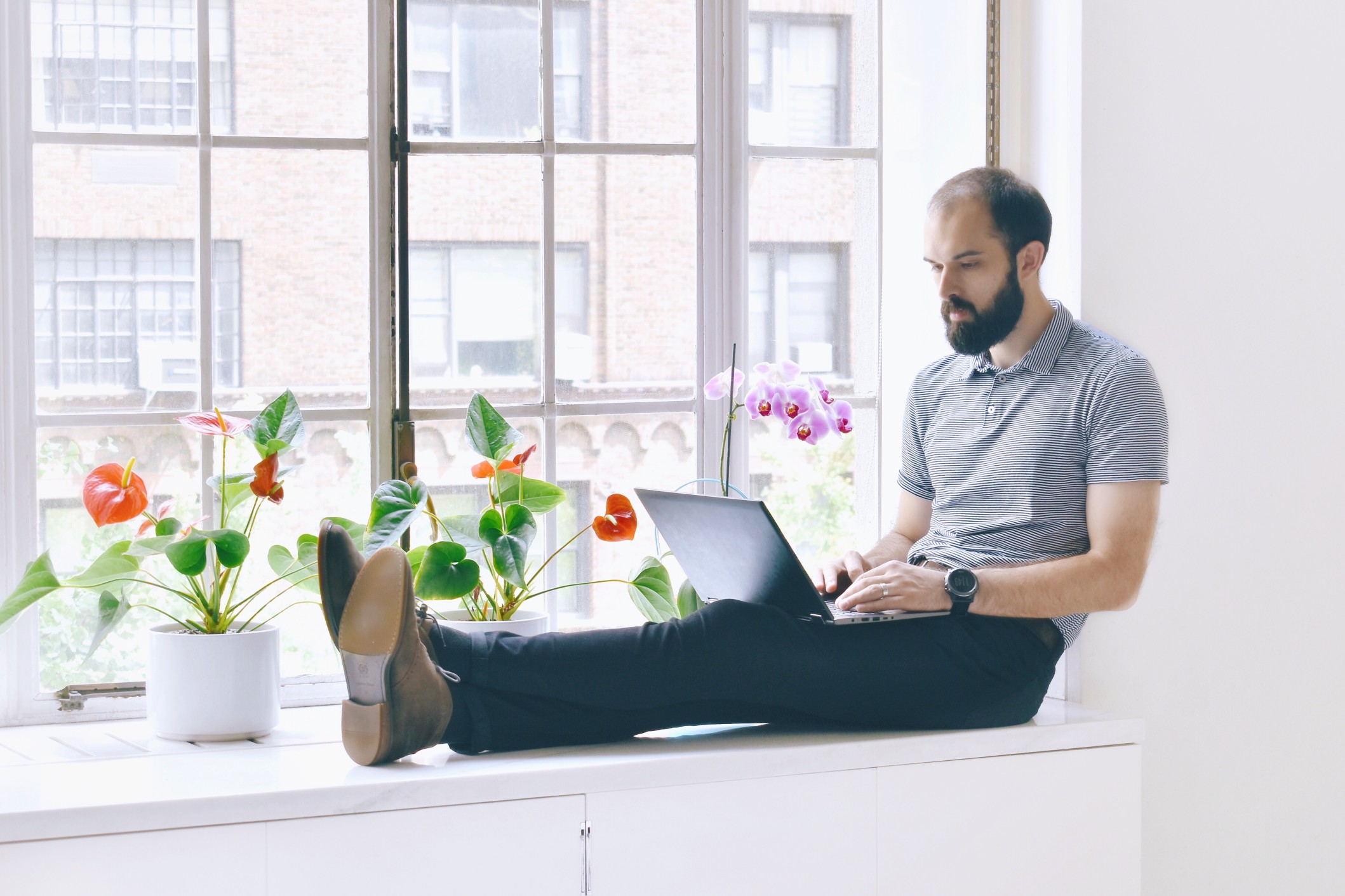 freelance writer working on laptop sitting on windowsill