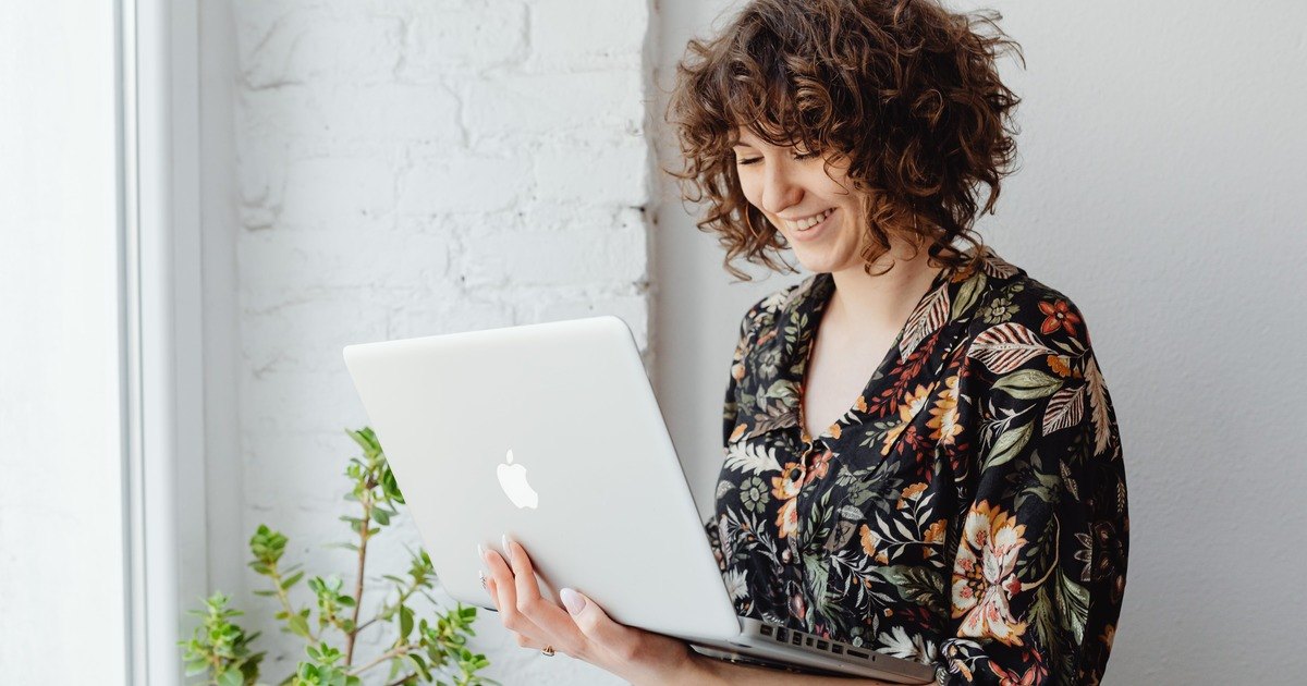 Writer holding laptop standing near plant