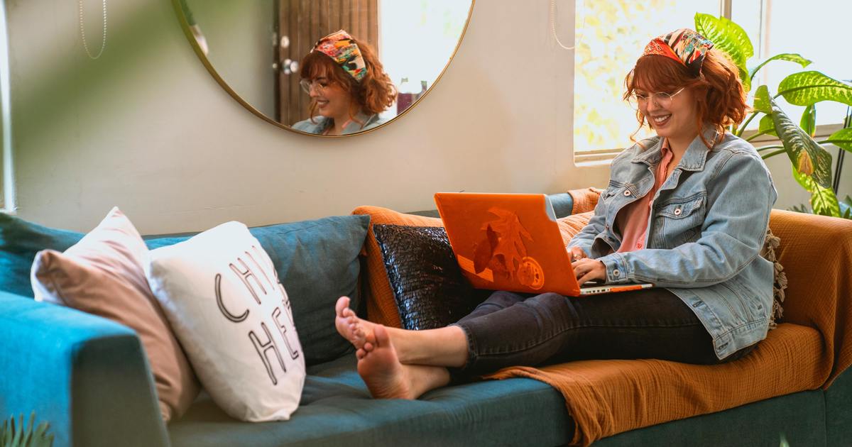 Writer sitting on couch typing on a laptop