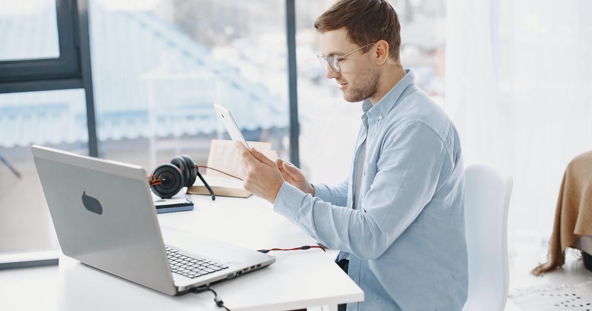 Writer holding tablet while working at a desk with laptop