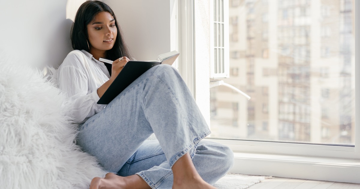 Woman writing in notebook while sitting by window