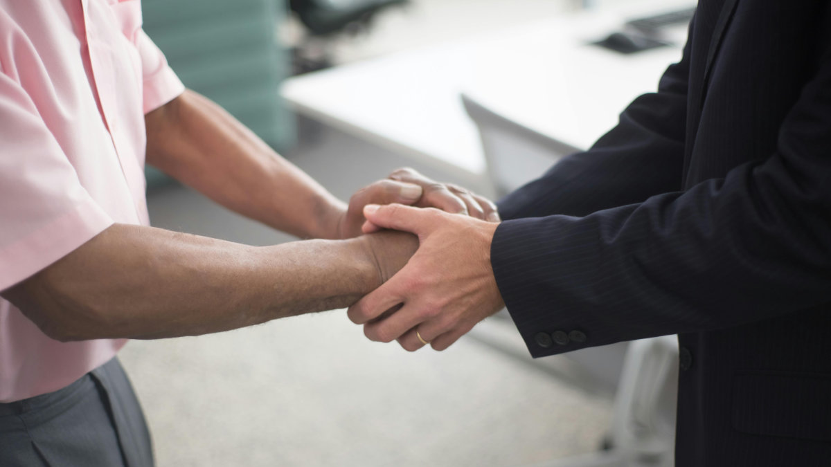 Two people standing and holding each other’s hands in a supportive, reassuring gesture in an office setting.