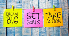 Three sticky notes displaying the three phrases Dream Big, Set Goals, and Take Action hung on a string