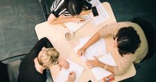 Overhead photo of three businesswomen sitting at a table with papers, notepads, and pens