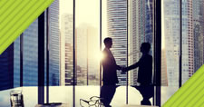 Office conference room table with pens, paper, eyeglasses, and water glass near colleagues shaking hands in front of large windows