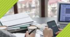 two colleagues' hands working at a desk with paperwork, mobile phone, and laptop