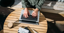 Overhead photo of a woman sitting at an outdoor table typing on a laptop computer