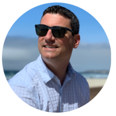 Man on beach smiling with sunglasses and light blue button down shirt