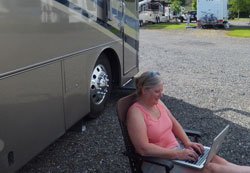 Christine Butler sitting on the ground with a laptop next to an RV