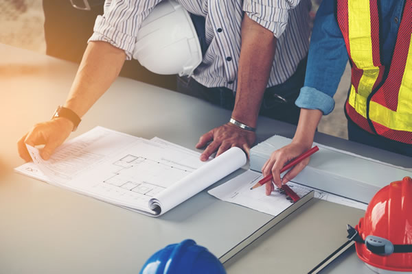 Two construction workers at a desk looking over a blueprint