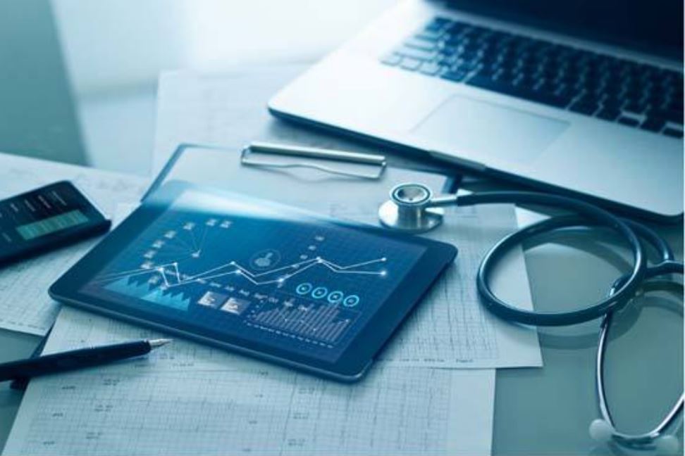 A medical office with a tablet, paperwork, and laptop on a desk